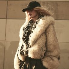 A woman wears a black baseball cap, and fur jacket.