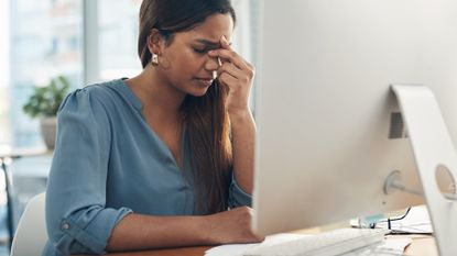 Woman suffers from eye strain at her work computer desk