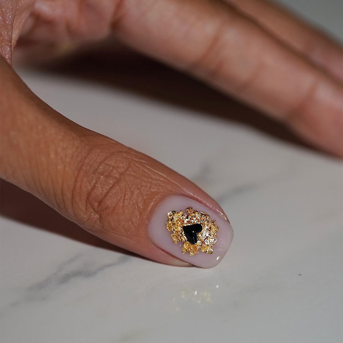 A manicure with a gold foil heart detail by Iram Shelton