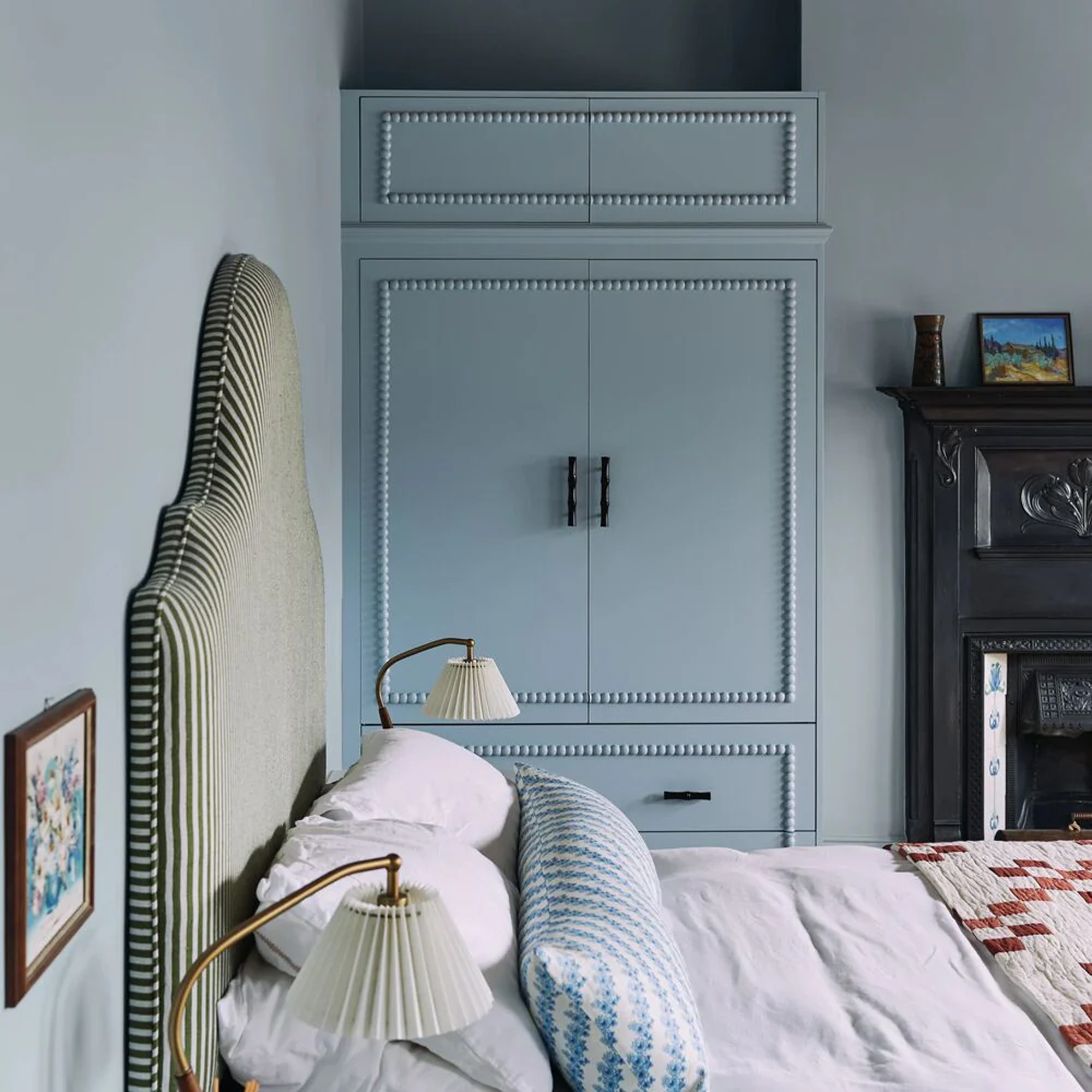 A bedroom with a large patterned fabric headboard and walls painted in COAT Paint's pale blue Lie In colour