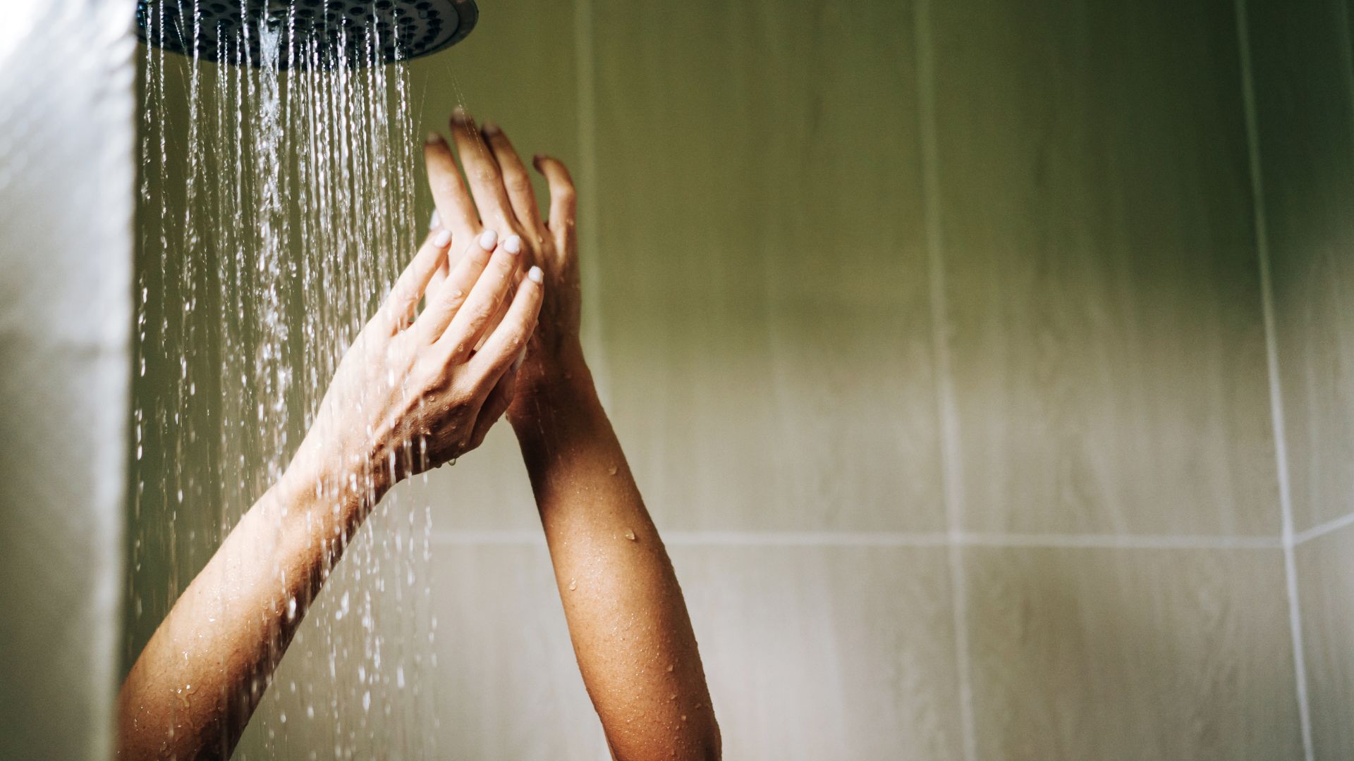 A person stands in a shower with their arms raised. The bathroom has light wood-effect panelling on the wall.