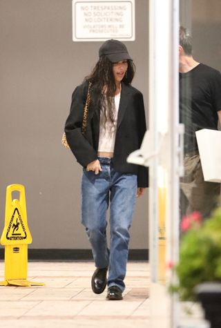 Zoë Kravitz wears a black baseball cap, a white t-shirt, black blazer, baggy jeans, black loafers, and a slouchy Saint Lauren bag in leopard while leaving dinner with Yves Saint Laurent's Anthony Vaccarello in West Hollywood, California.