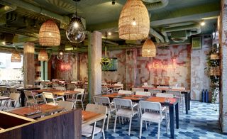 Restaurant with tables, chairs, bar, patterned coloured walls and large pendant lights at Bar Skuka, Frankfurt, Germany.