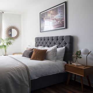 Bedroom with grey upholstered bed with many pillows with a framed picture of Hong kong above bed and a framed mirror on the wall