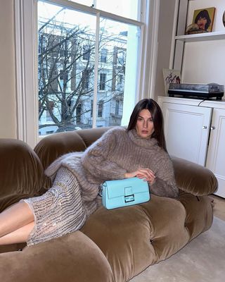 @camillecharriere wearing a beige jumper and sequin skirt on a sofa