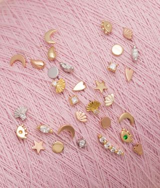 Gold ear studs against a pink background