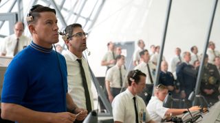 photo from a movie set showing a man in a blue t-shirt standing next to a handful of other men in white dress shirts and black ties