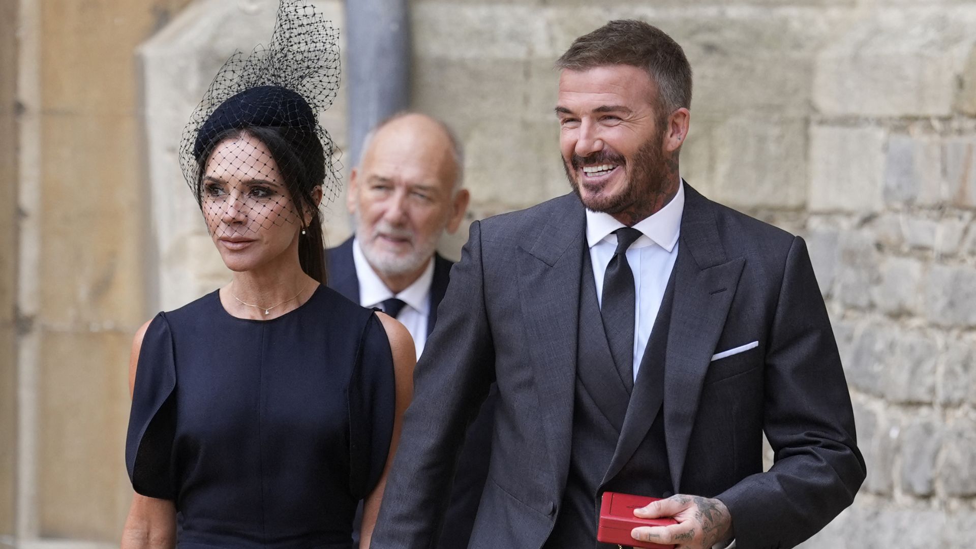 Victoria Beckham walks hand-in-hand with David Beckham, wearing a navy dress with black croc-print heels and a black croc bag.