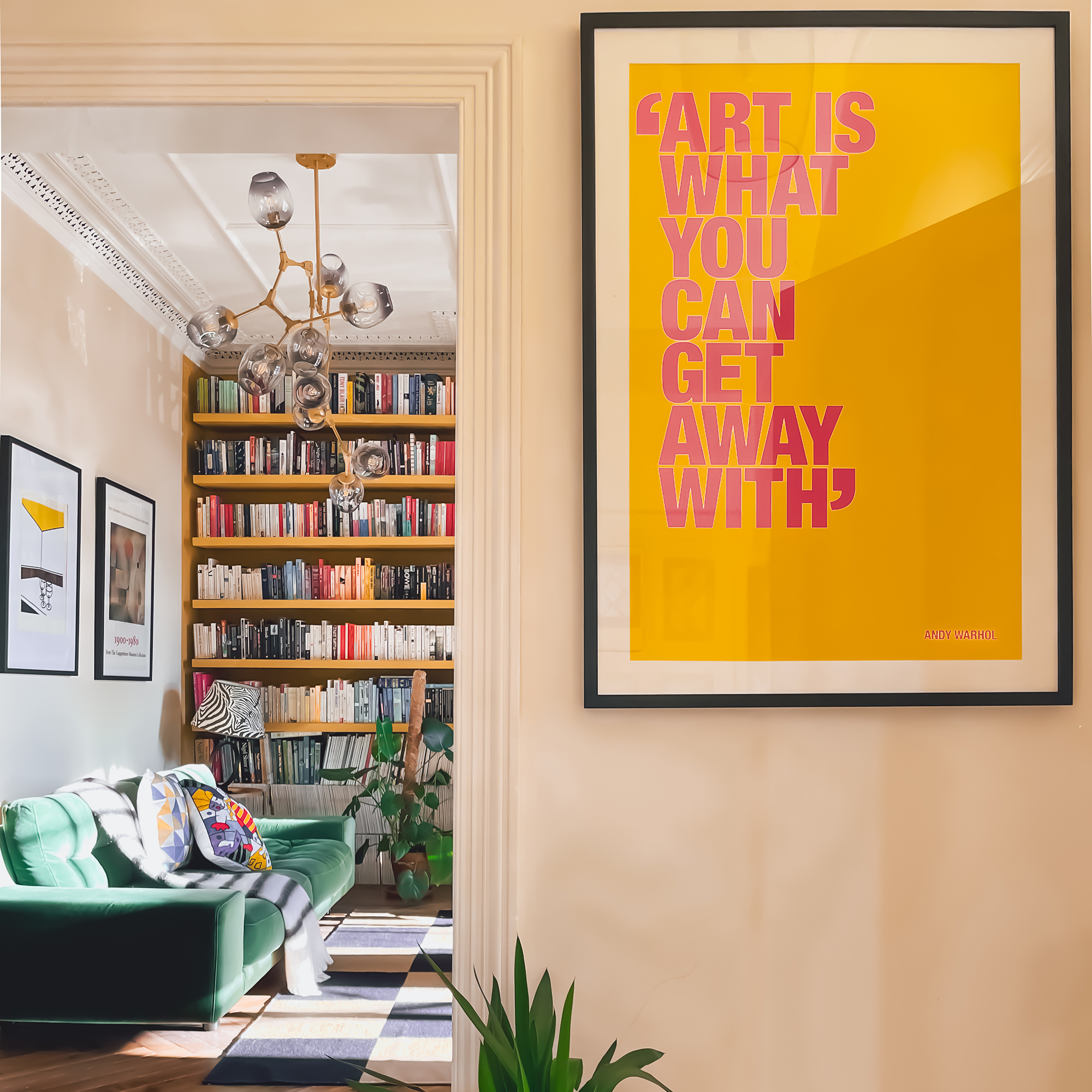 Doorway into a living room with floor-to-ceiling bookshelves and green velvet sofa, with framed art print in the foreground