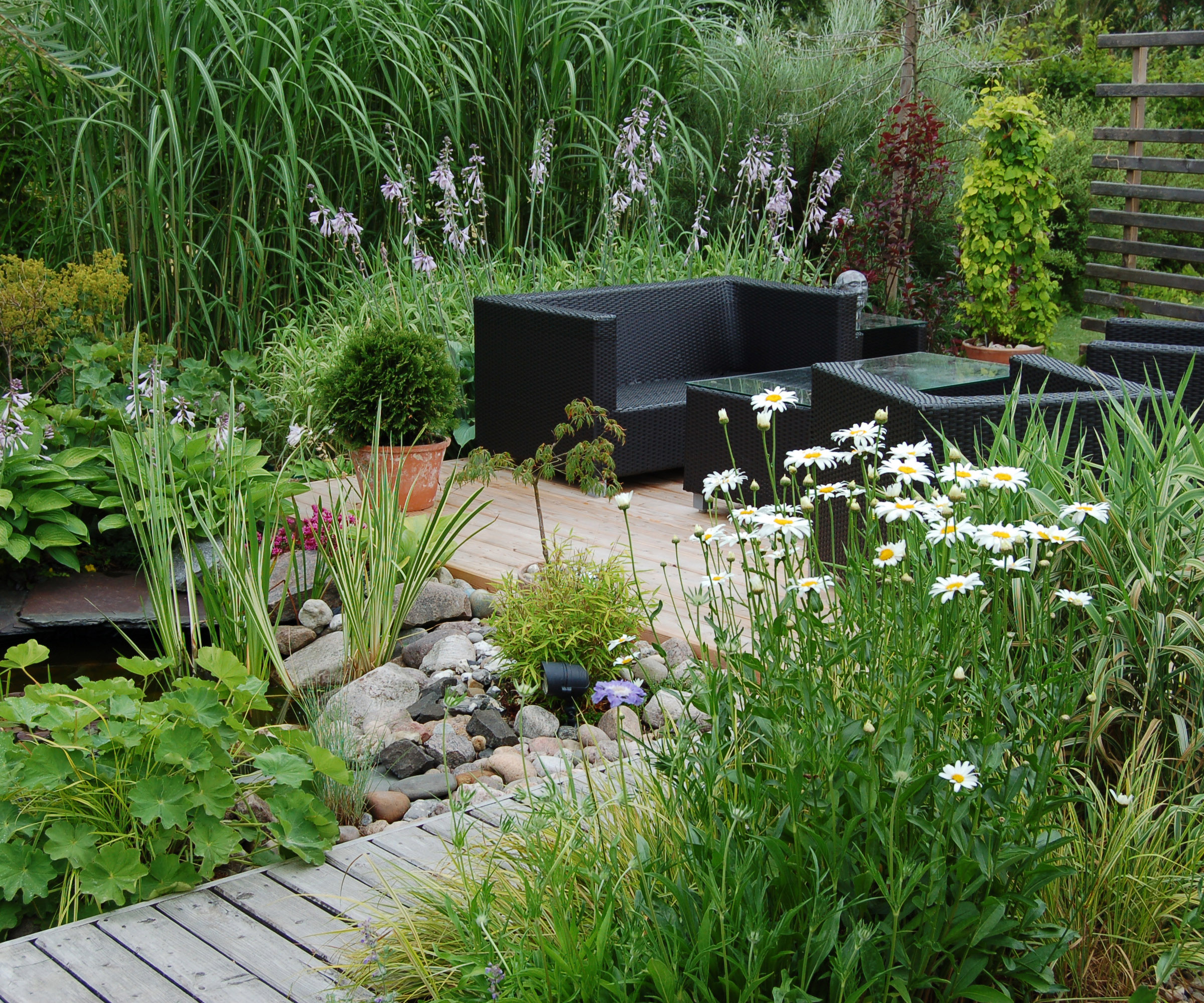 Outdoor garden lounge with a pond and a modern wicker sofa and wooden decked pathway