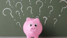 A piggy bank sitting in front of a chalkboard covered in question marks.