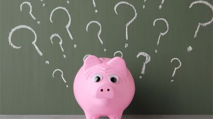 A piggy bank sitting in front of a chalkboard covered in question marks.