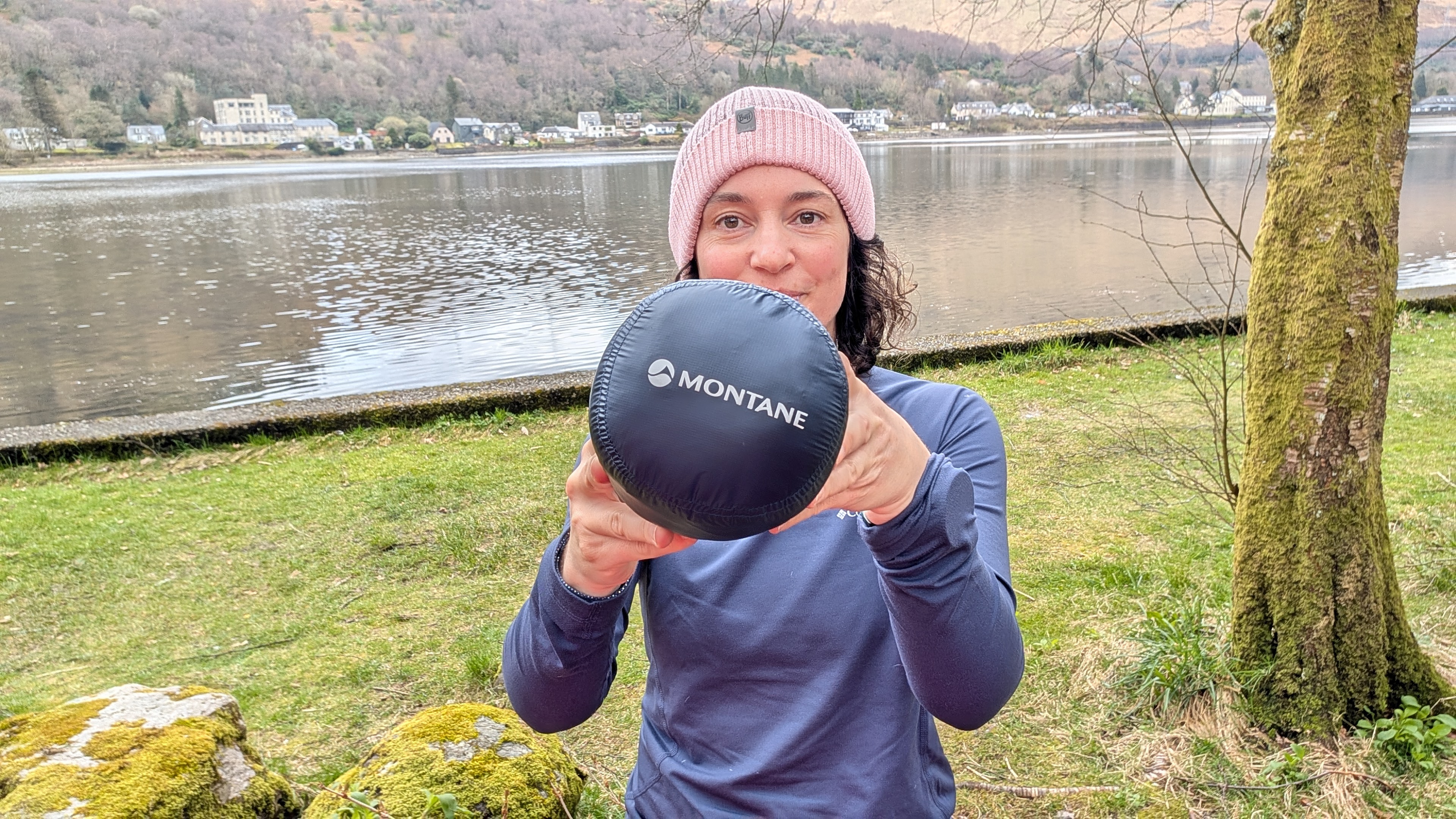 A woman hiker holds up her Montane Alpine Nano 850 down jacket packed in a stuff sack