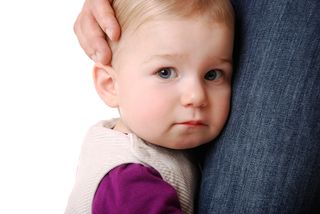 A toddler girl clings to her mom.