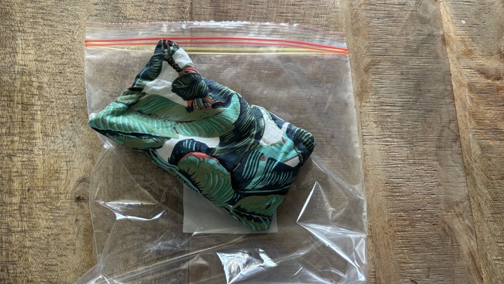 A tropical-patterned eye pillow in a freezer bag on a wooden table.