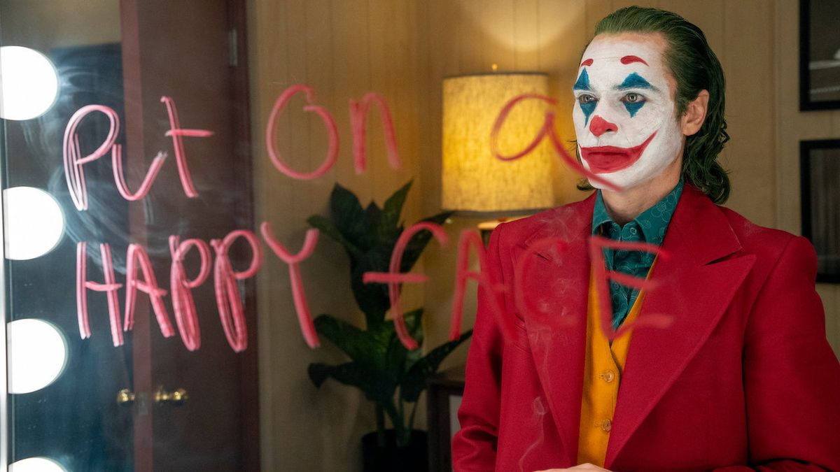 Joaquin Phoenix as Arthur Fleck in clown makeup and &#039;put on a happy face&#039; on a mirror in red in Joker