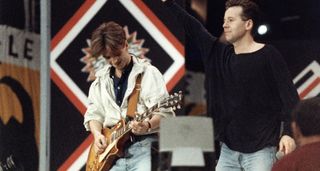 Simple Minds' Charlie Burchill [left] and Jim Kerr perform at Nelson Mandela's 70th Birthday Party concert. Burchill plays a Gibson Les Paul Standard and wears a white jacket.