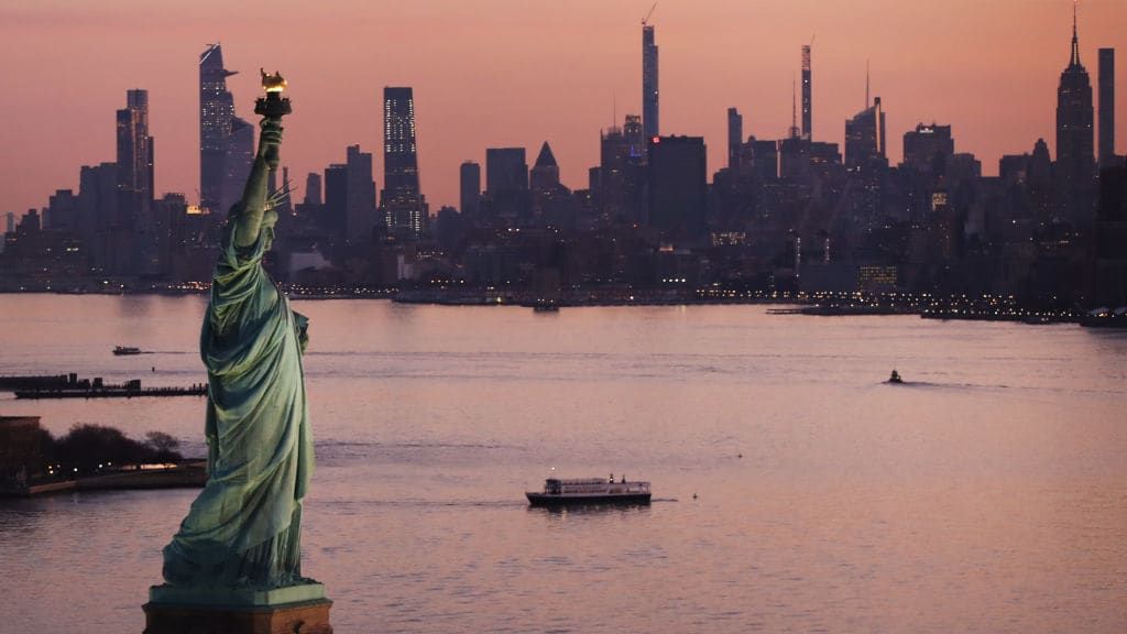 The Statue of Liberty and New York City skyline at dusk.