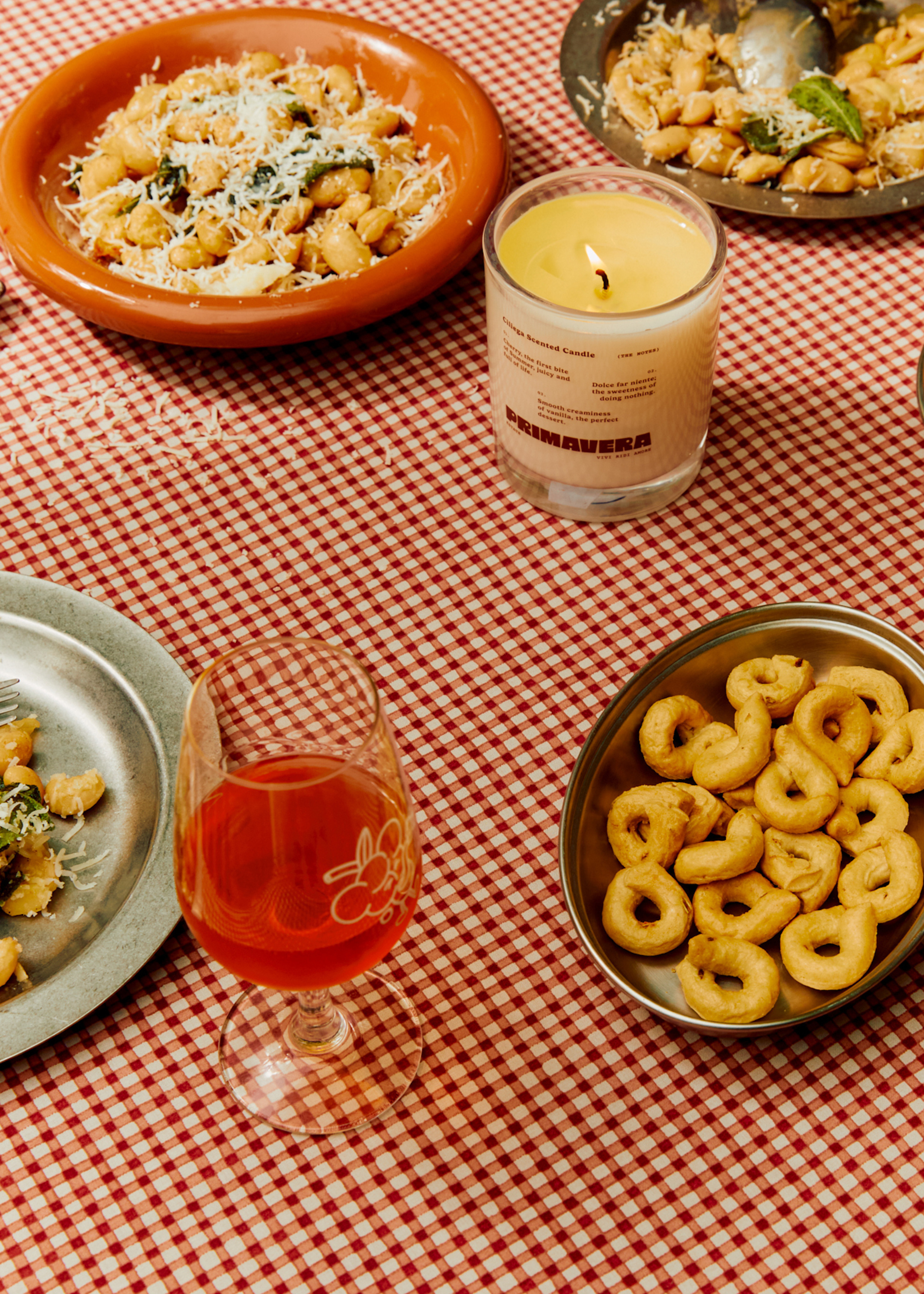 A table with plates of food by a glass of aperol and a cherry-scented candle from Earl of East