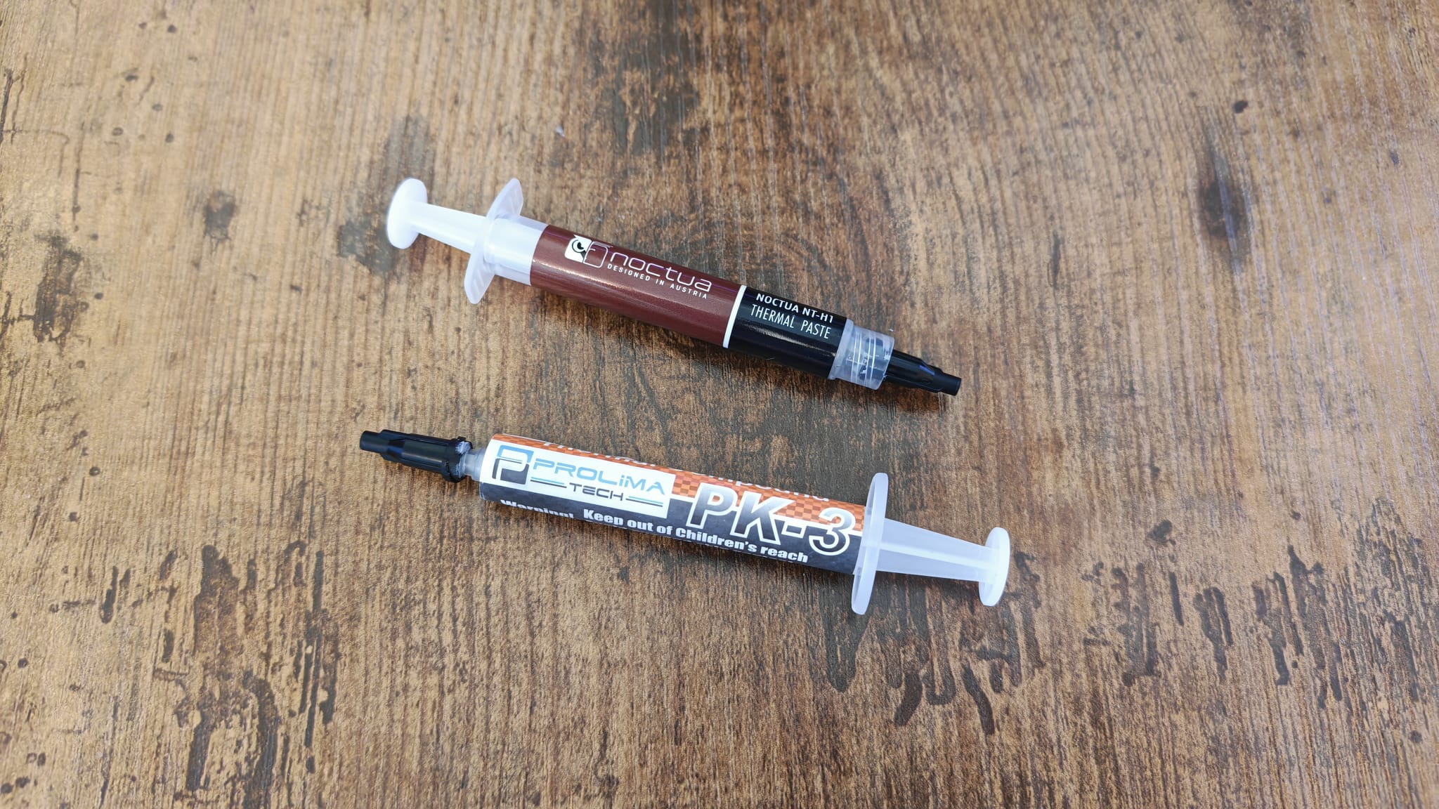 Two types of thermal paste lying on a wooden gaming desk surface