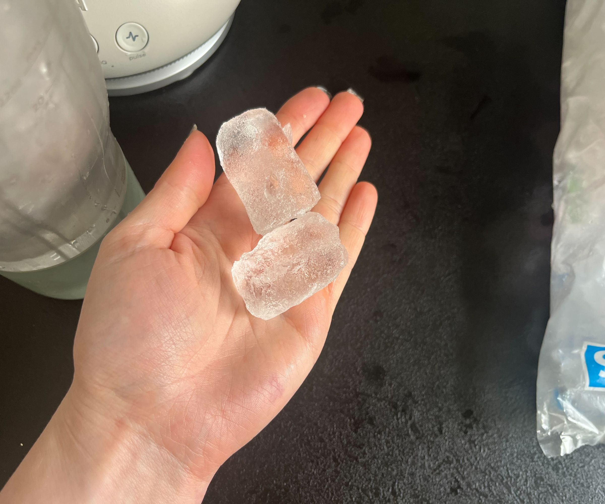 Two large ice cubes on the palm of someone's hand above a black counter