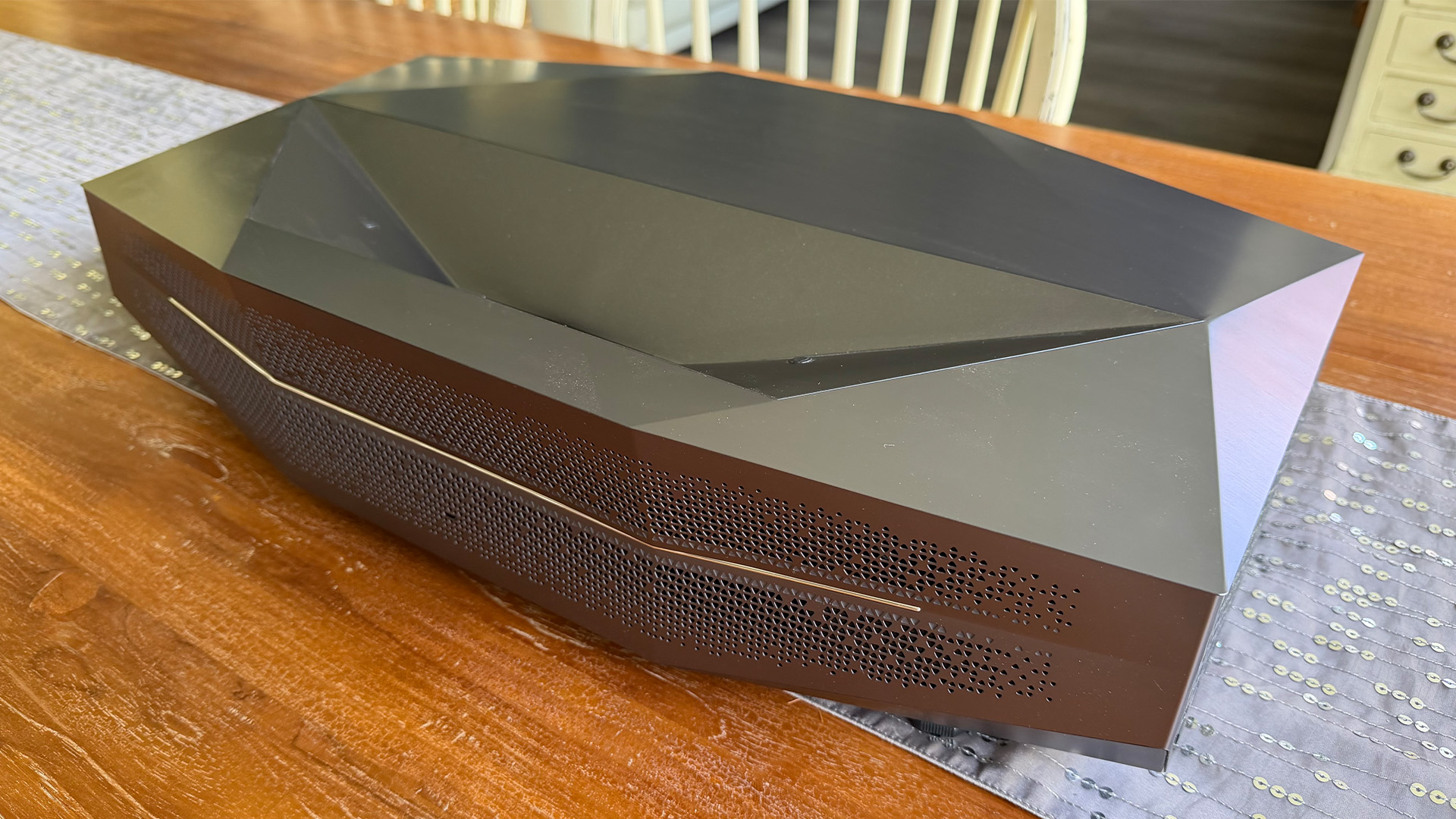 AWOL Vision Aetherion Max ultra short throw projector on grey runner on wooden table slight angle from right