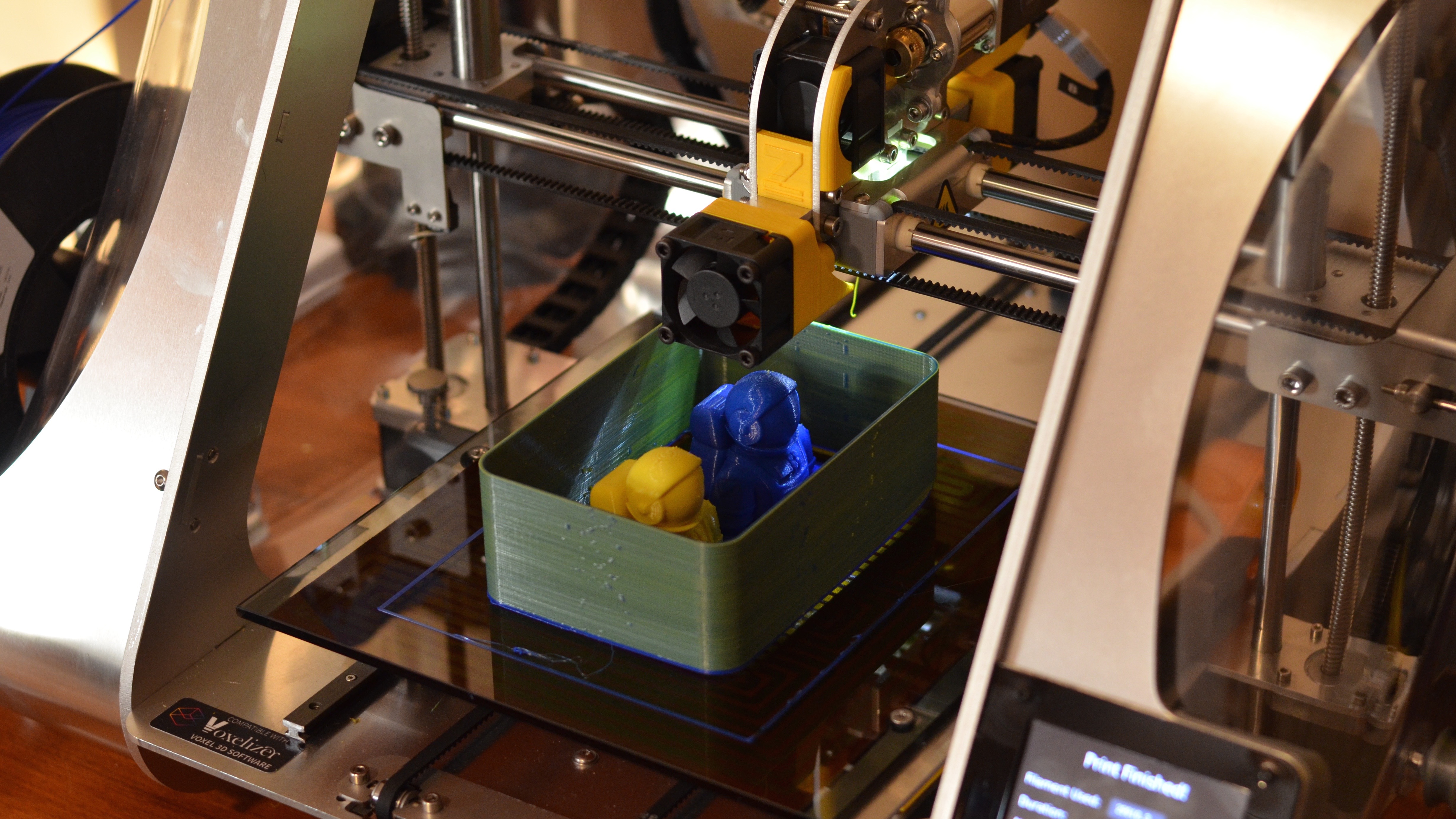 When printing in two colors using the ZMorph's optional Dual Pro toolhead, the print head needs to be cleaned between each color change. The result is the removable wall surrounding the astronaut models, which in this case takes on a greenish hue from alternating between the blue and yellow filament colors.