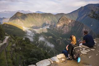 A man and a woman watch the sunrise at Machu Picchu