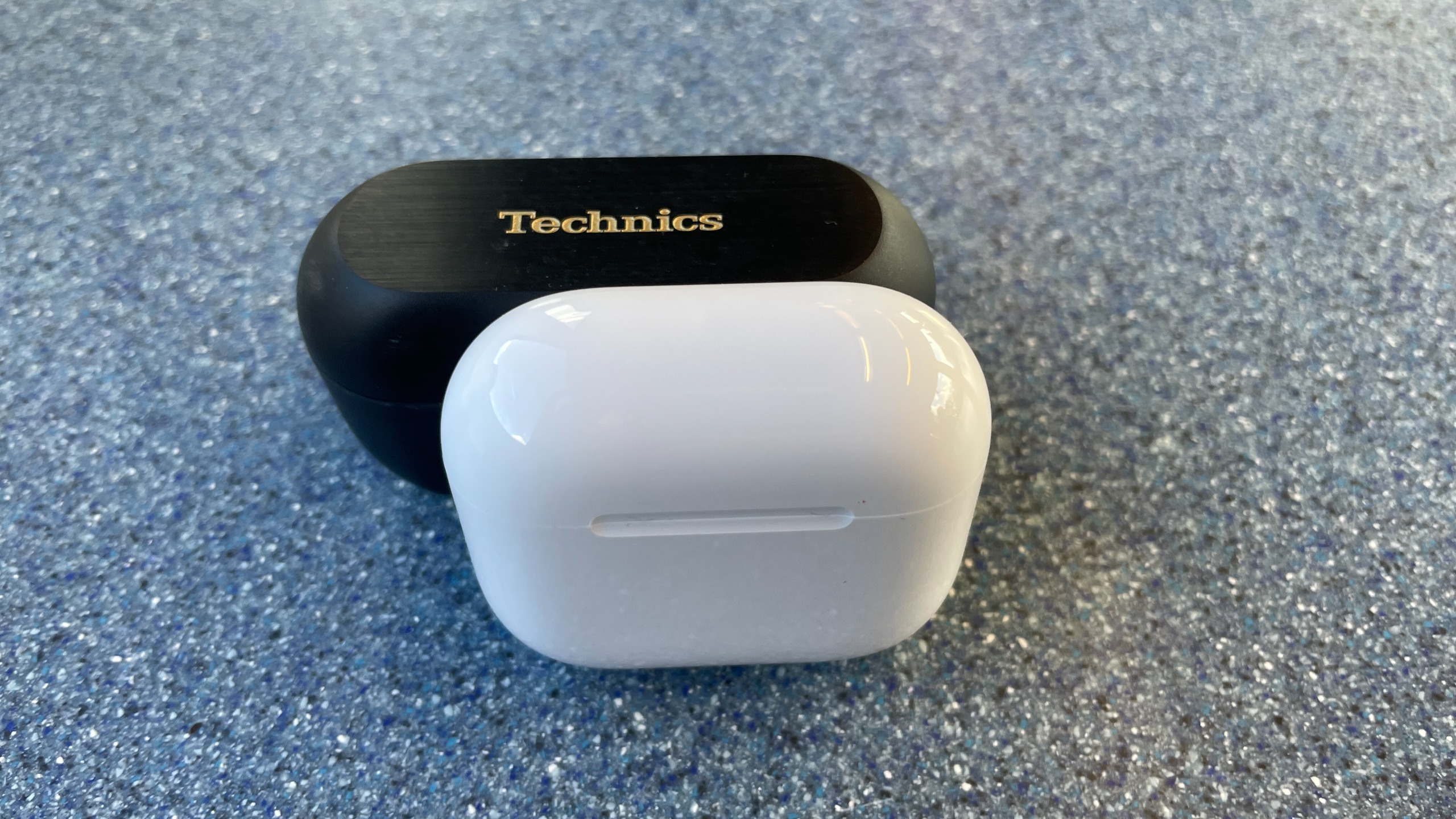 Apple AirPods 5 with Wireless Charging, on a blue table and held in a hand