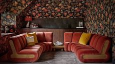 converted loft with orange velvet wraparound seating and floral wallpaper in dark colours