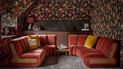 converted loft with orange velvet wraparound seating and floral wallpaper in dark colours