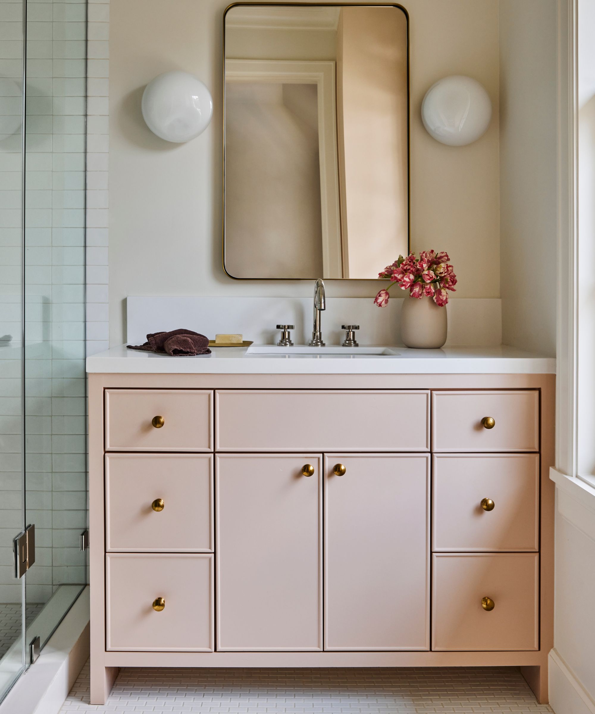 A bathroom with white mosaic tiles on the floor and a light pink vanity