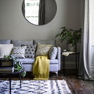grey living room with a big center circle mirror above a grey sofa with patterned pillows and a black circle coffee table on top of a patterned rug
