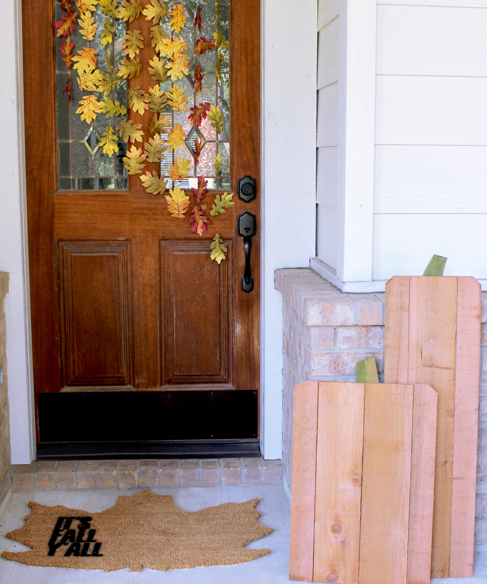 a porch with fall garland on door, doormat and wood pumpkins - Gray House Studio