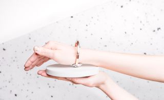 A pink brass band bracelet is displayed on a woman's hand.