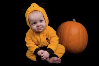 Baby dressed in a costume next to a Halloween pumpkin.