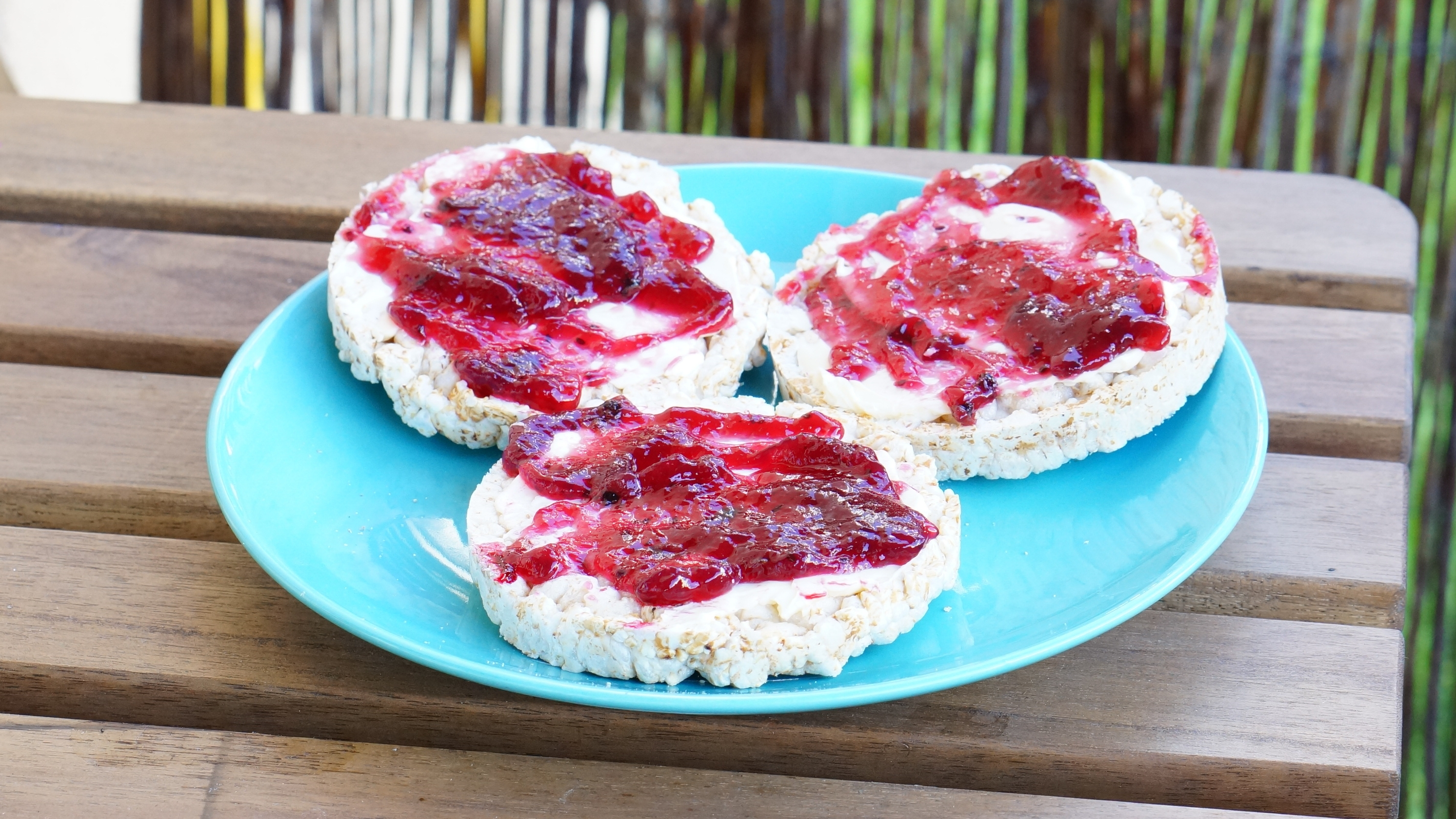 Three rice cakes with jam on top sit on a blue plate on a wooden table
