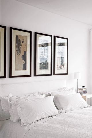White bedroom with artwork framed in dark wooden frames above the bed