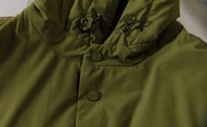Close up image of a green hooded sweater, green buttons and toggles, grey background
