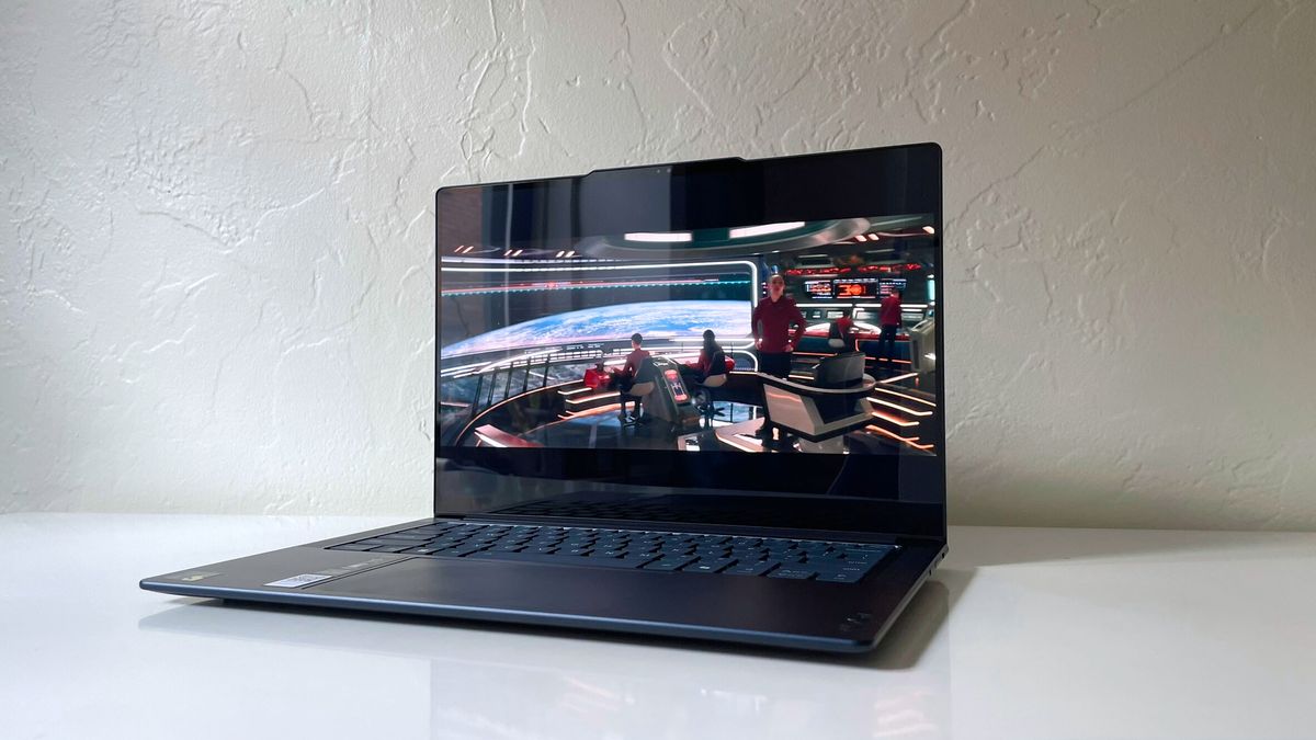 An angled view of an open and powered on laptop on top of a white surface; a scene from a movie is displayed on its screen.