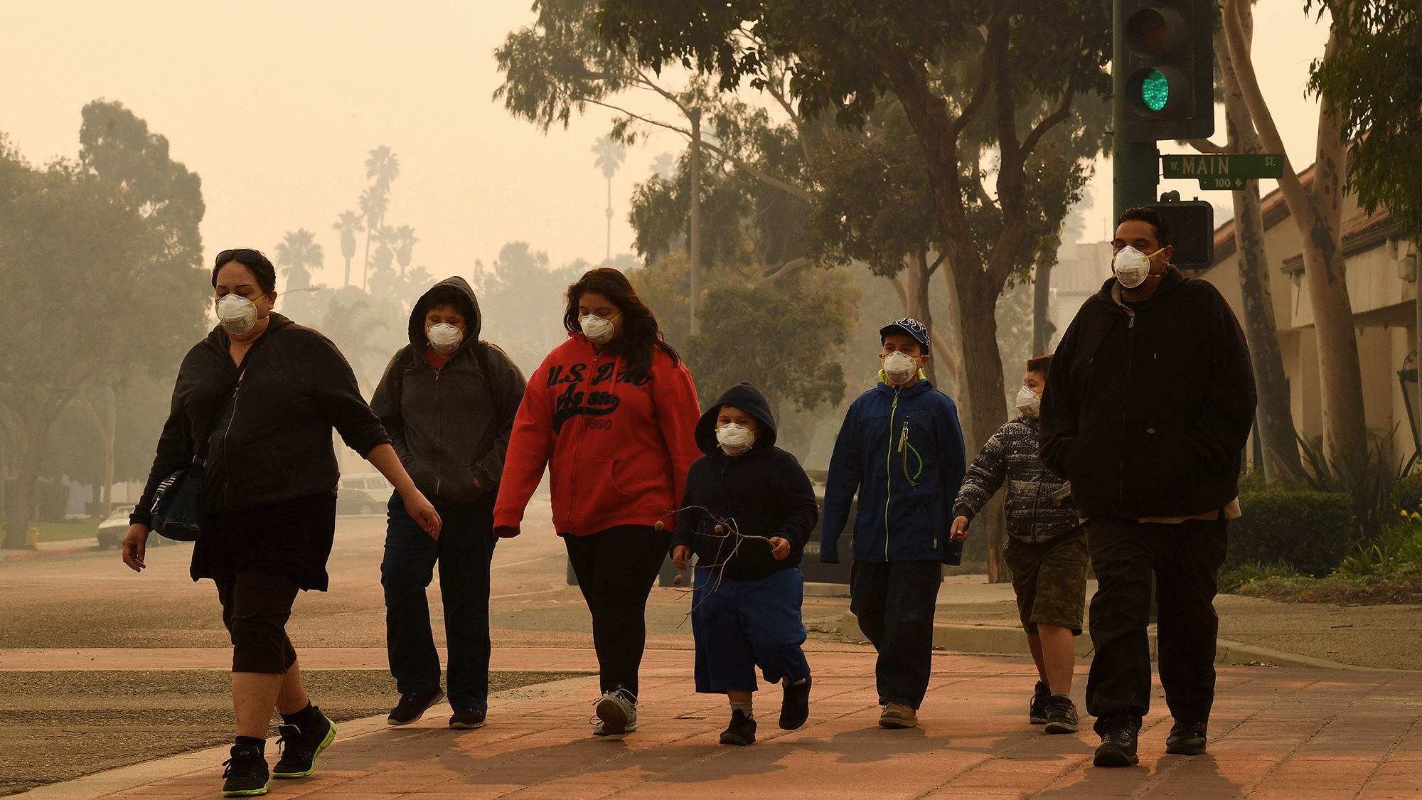 A group of people wearing white face masks walk down a hazy street.