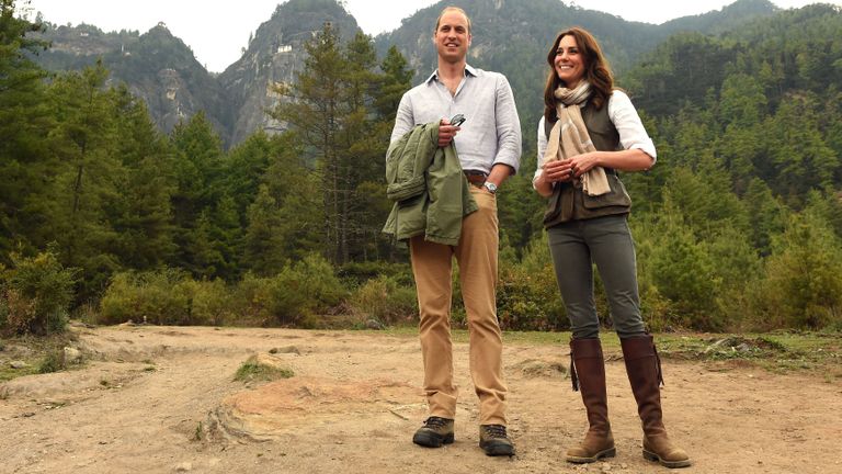 Prince William and Kate Middleton stand together in a forest clearing.