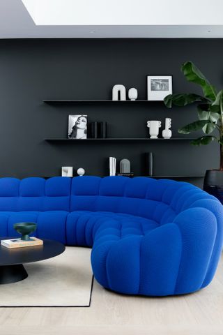 A cobalt blue curved sofa and dark walls with white decorative objects