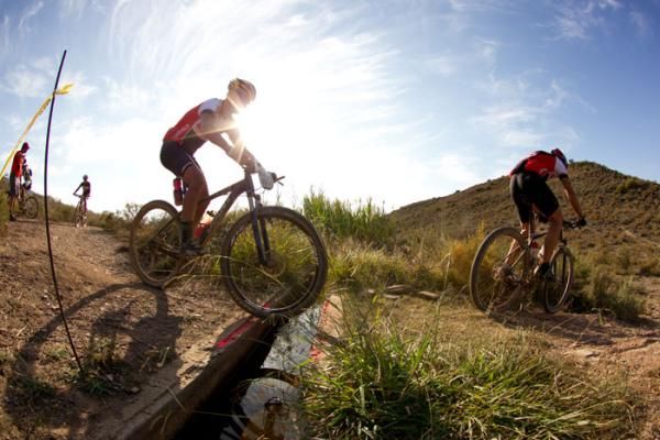 Riders jump over an irrigation ditch during stage 2