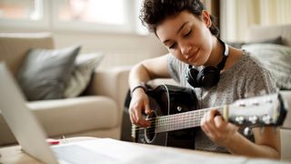 Young woman playing acoustic guitar in front of laptop