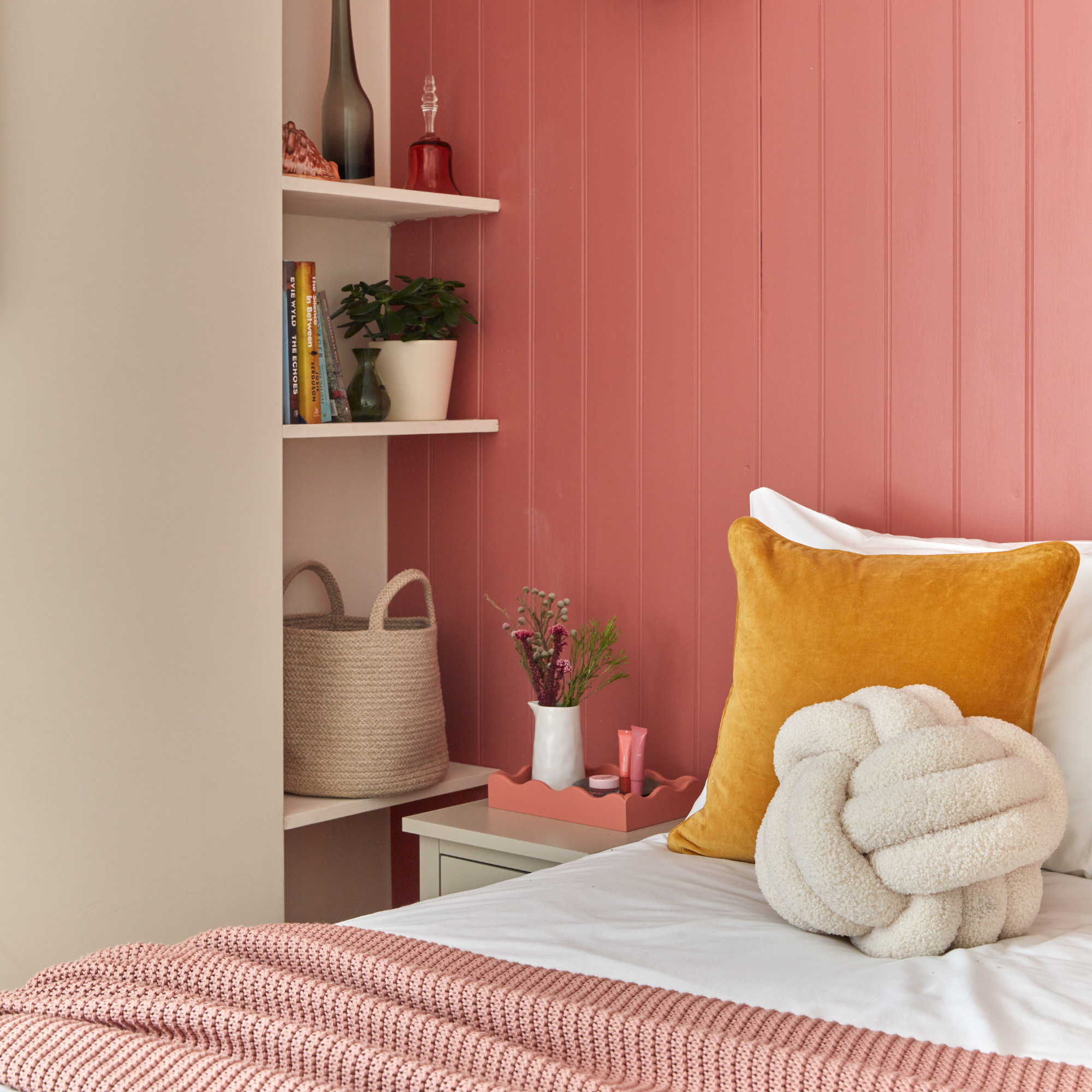 Bed with white sheets and red throw infront of a terracotta wooden pannelled wall.