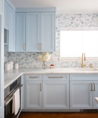 A coastal kitchen with blue cabinets, white marble countertops, and stained-glass mosaic tiles covering the walls in the same color palette