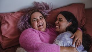 A couple smiling and laughing as they share a cuddle in bed