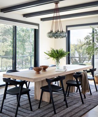 Neutral dining room with large windows and a simple and sculptural wooden dining table with black chairs