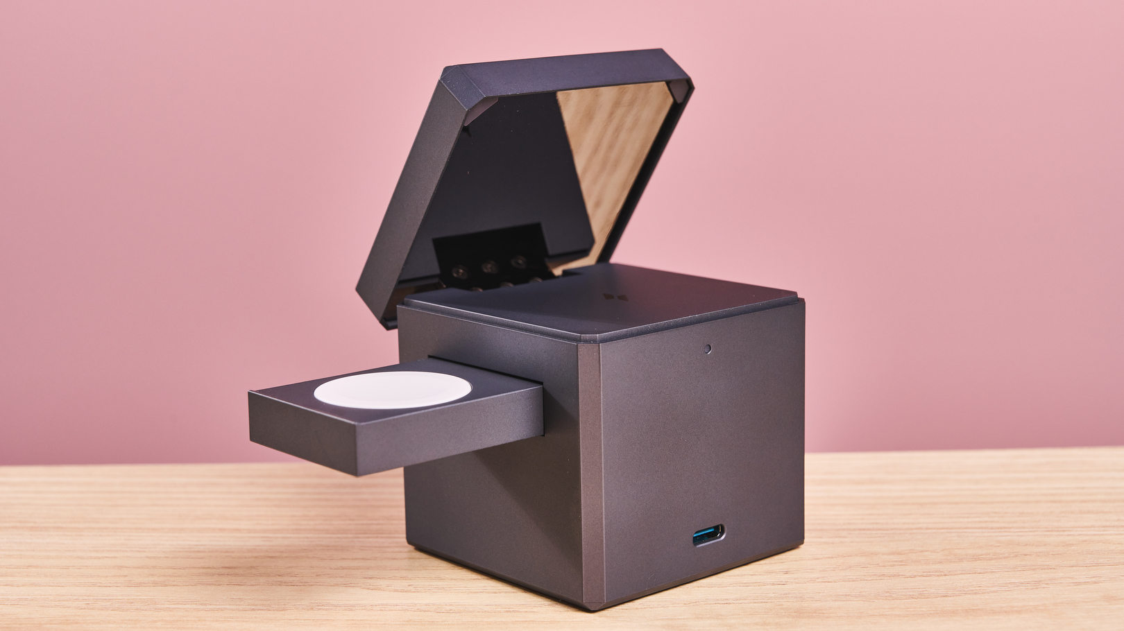 The image shows the back of the Anker 3-in-1 Cube with MagSafe, the charging pad is raised at an angle, revealing the reflective surface on its reverse. The AirPods charging area had been revealed on the top of the cube, and the Apple Watch charger pop-out is extending from the left-hand side of the cube.